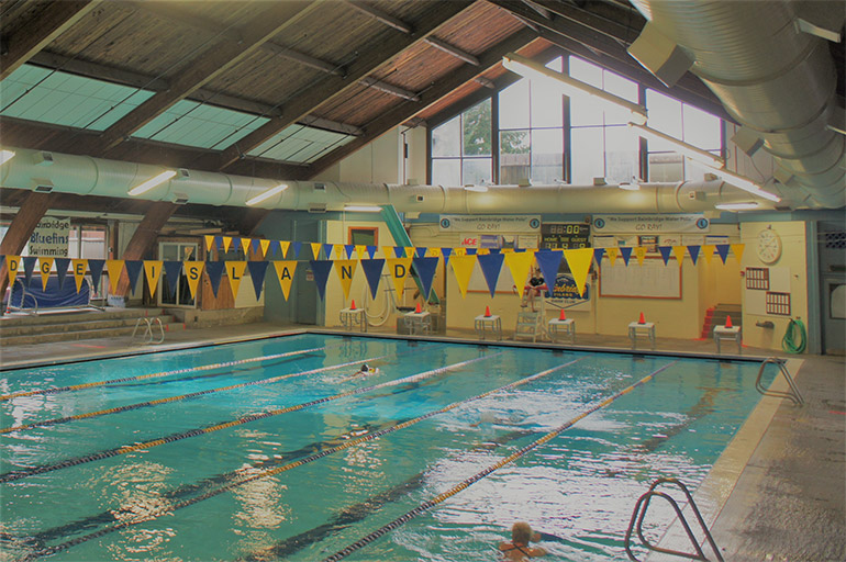 Inside of Ray Williamson Pool with flags above the racing lanes and a swimmer in one lane